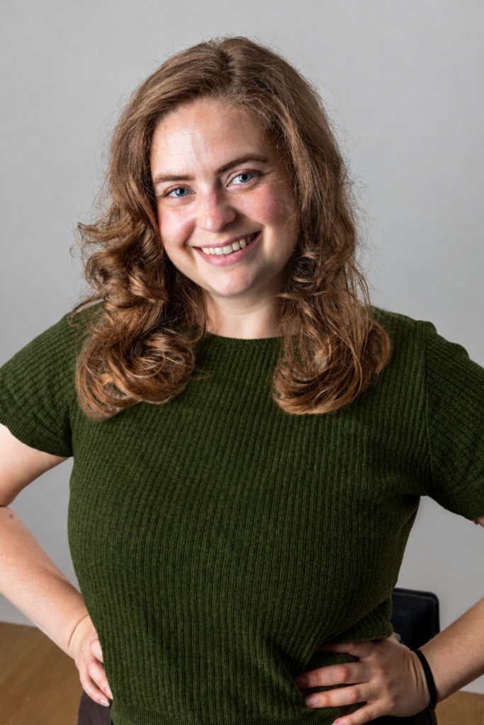 Photo of Katie Shultz in a dark green sweater with her hands on her hips.